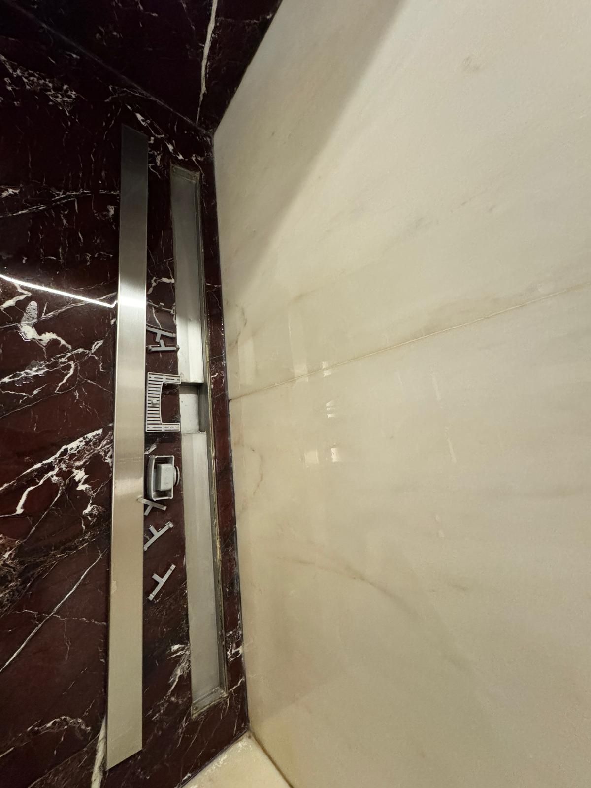 Porte dell'ascensore con finiture in acciaio inossidabile e marmo scuro a sinistra, marmo chiaro a destra.