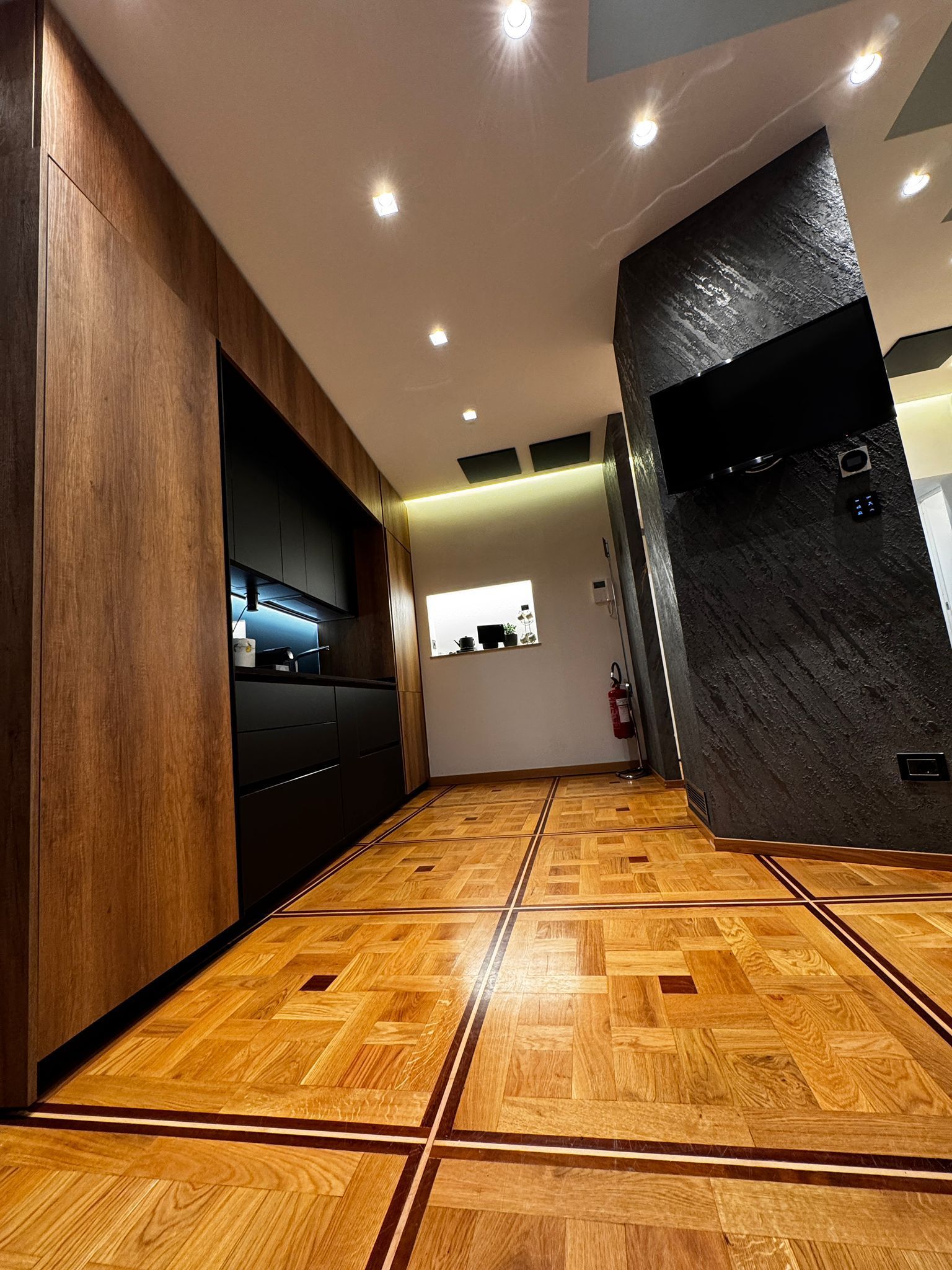 Interni moderni con pavimento in legno, mobili scuri, parete decorativa testurizzata e illuminazione da incasso.