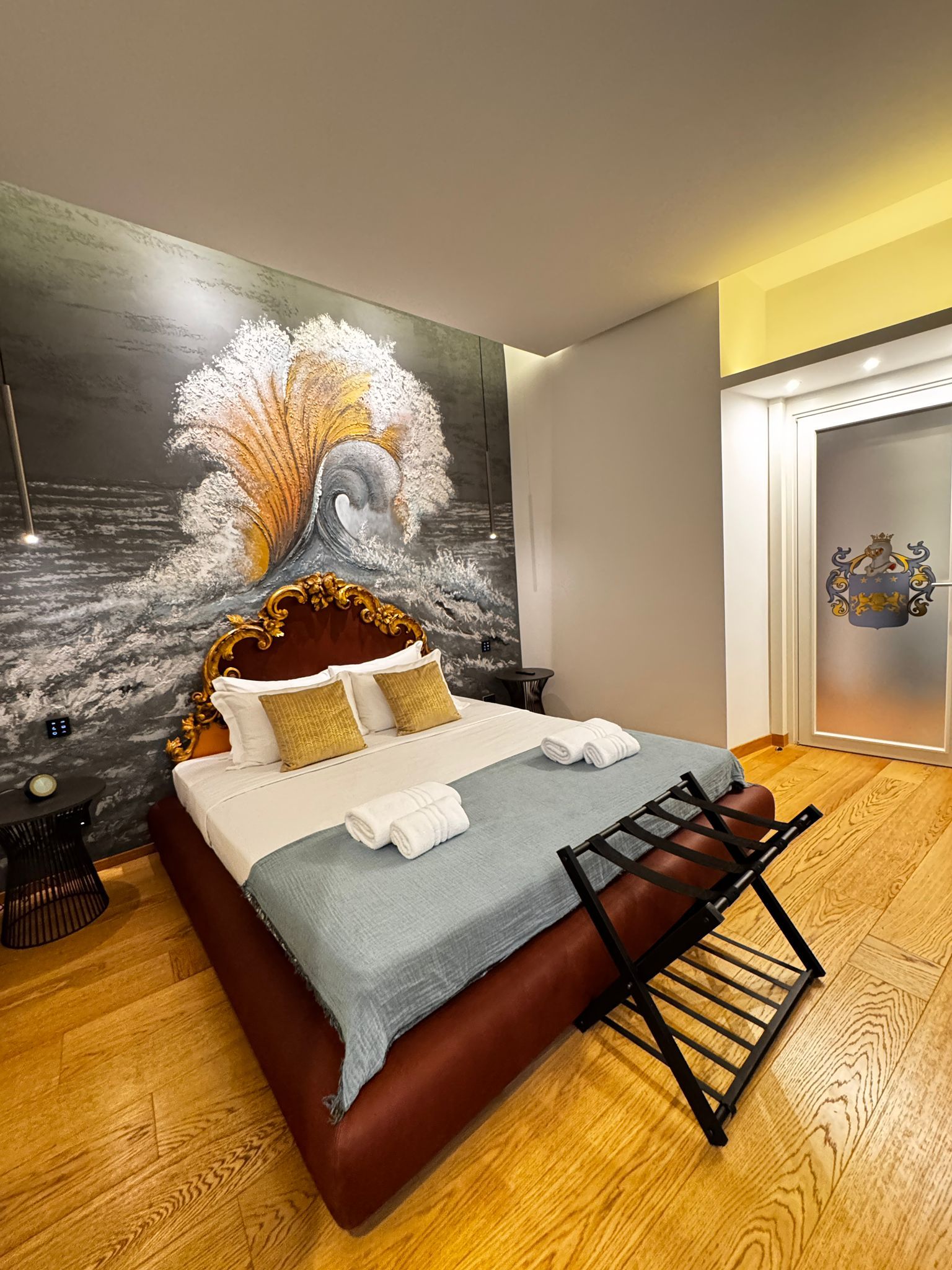 Camera da letto con un letto grande, pavimenti in legno e un murale dietro la testiera. Ai piedi del letto c'è un portavaligie.