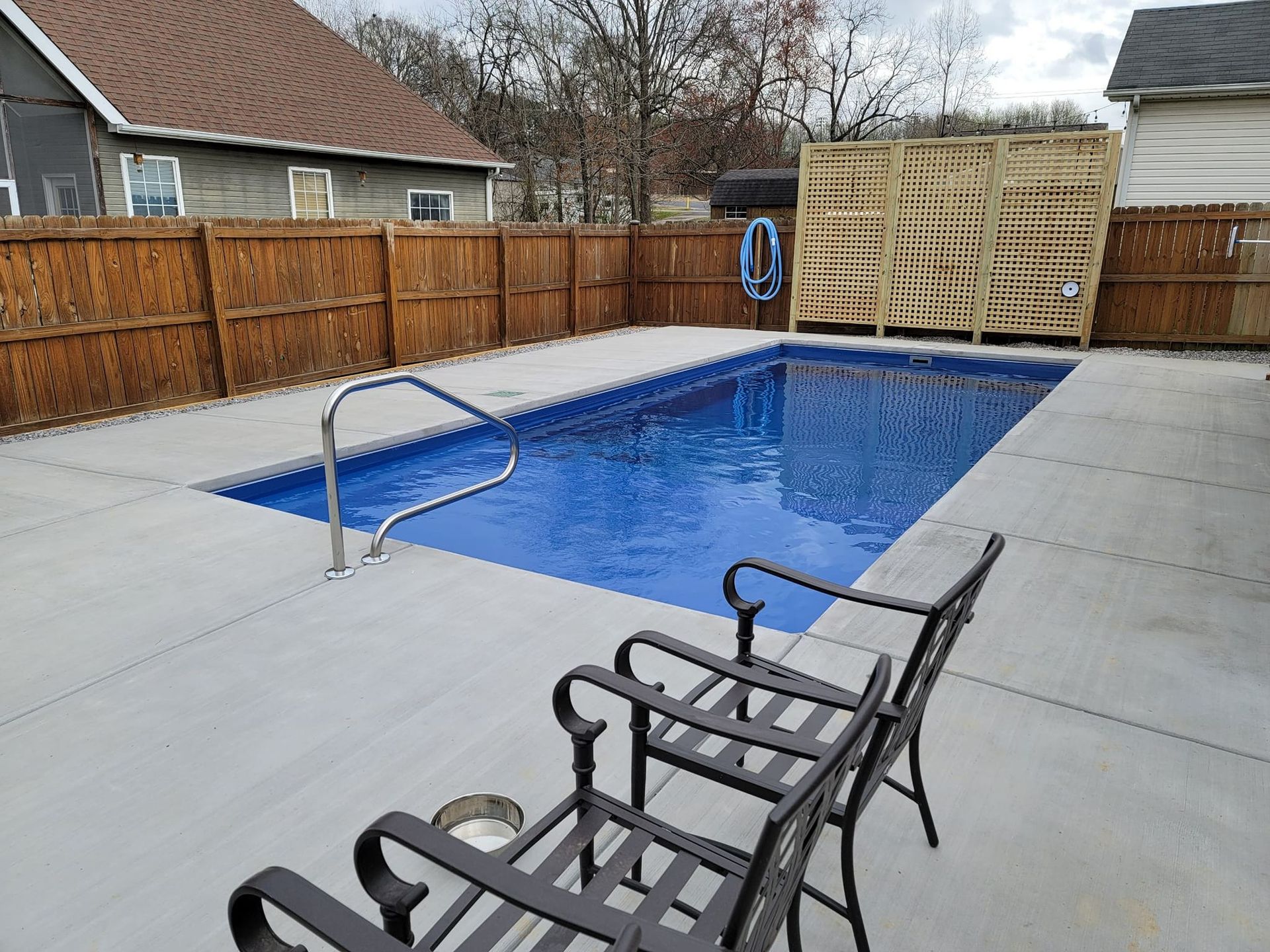 A large swimming pool is surrounded by a wooden fence and chairs.