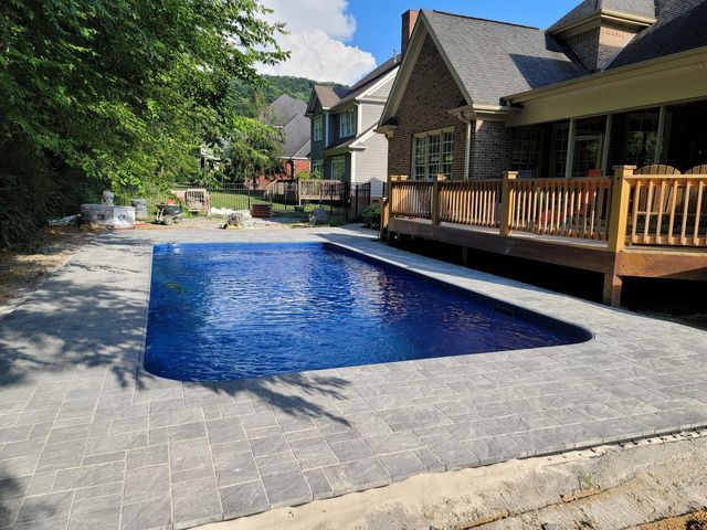 A large swimming pool is in the backyard of a house.