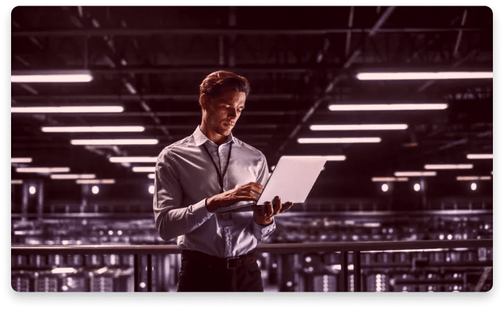 A man is standing in a dark room looking at a laptop.