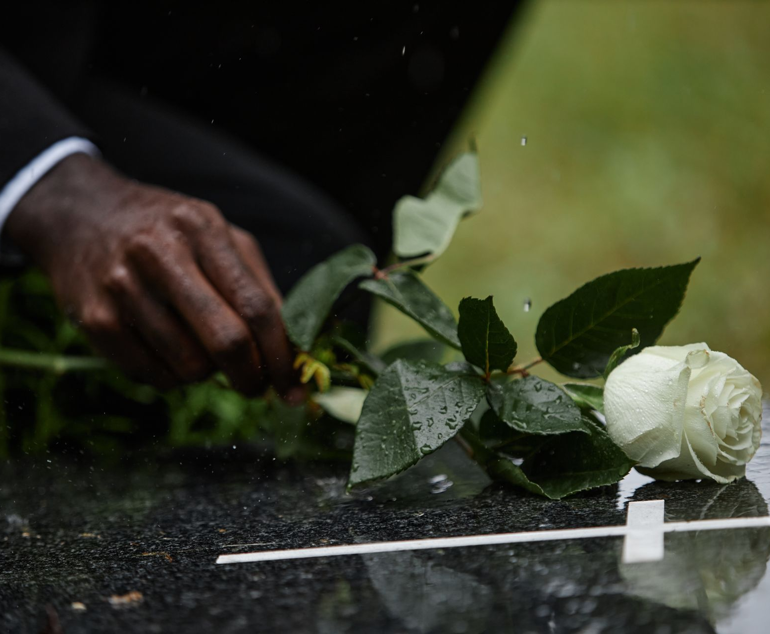 Person in black attire holding a red rose near a wooden coffin, with flowers arranged on top.