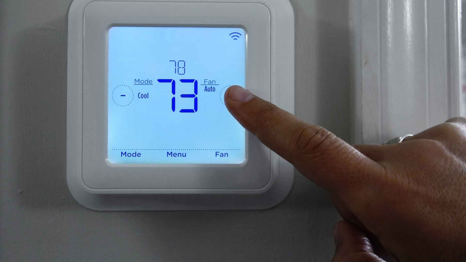 A person is pressing a button on a thermostat.