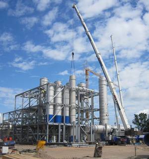 A large crane is lifting a pipe in front of a large building.