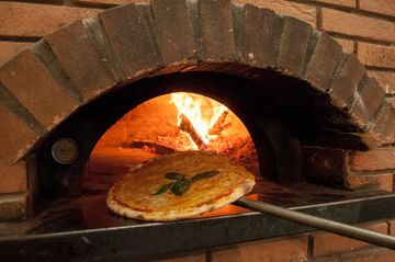 Una pizza viene tirata fuori da un forno a mattoni
