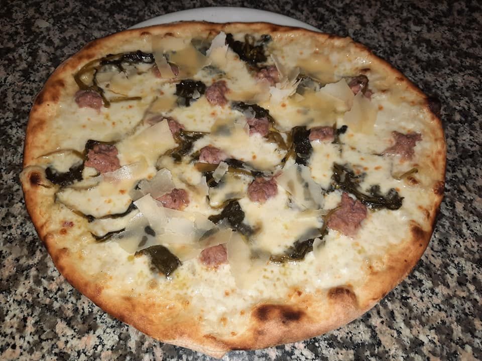 Pizza con salsiccia, verdure e formaggio, su un piatto bianco.
