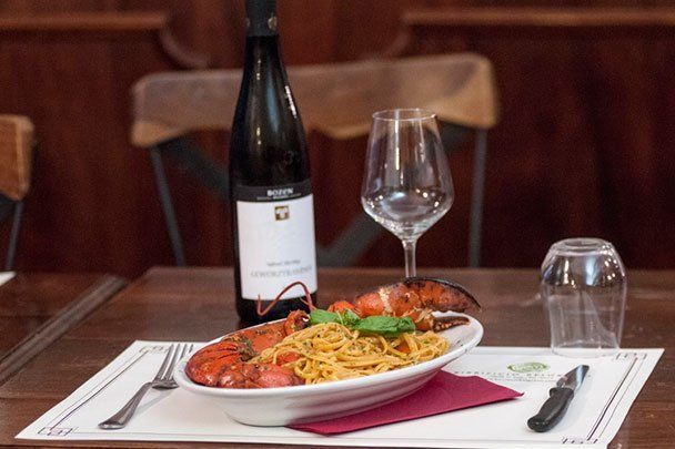 Piatto di pasta all'astice con vino, bicchiere e bottiglia su un tavolo.