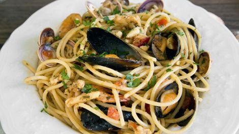 Un piatto bianco con sopra spaghetti e frutti di mare su un tavolo.