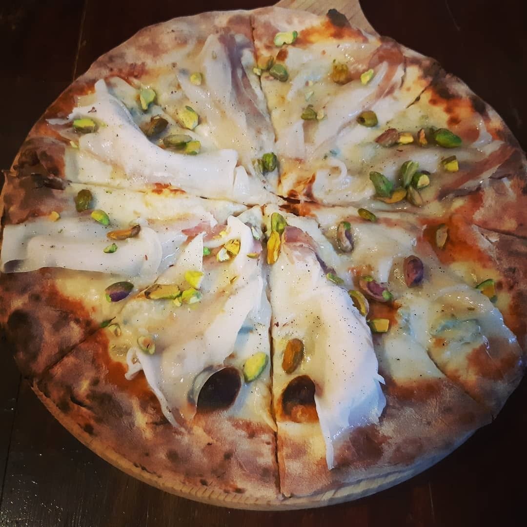 Pizza con condimento bianco e pistacchi verdi, tagliata a fette.