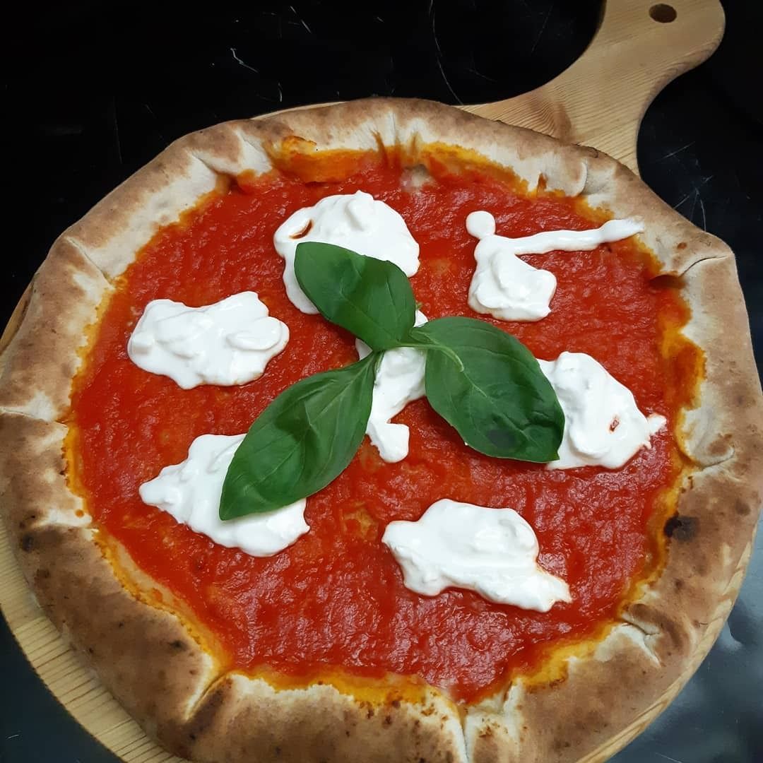 Pizza con salsa rossa, formaggio bianco e foglie di basilico su un tagliere di legno.