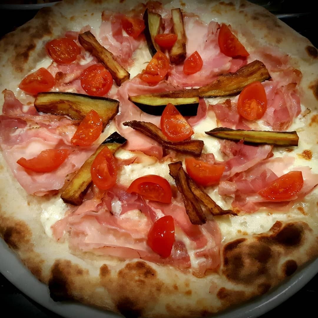 Pizza con prosciutto, melanzane arrostite e pomodorini.