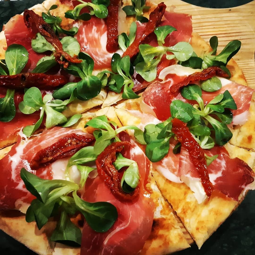 Pizza piatta con prosciutto, pomodori secchi e verdure.