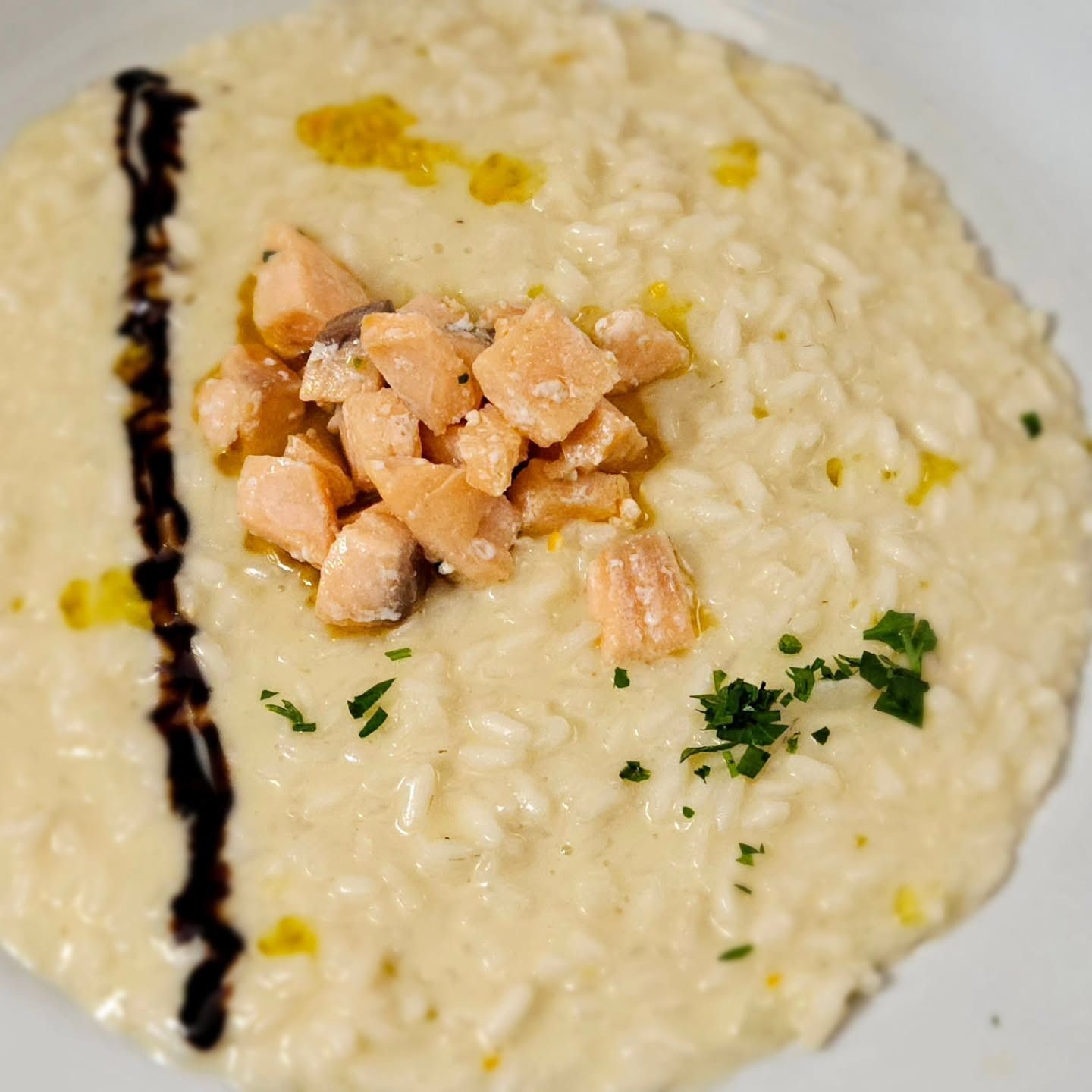 Risotto cremoso guarnito con pezzi di salmone, un filo di aceto balsamico e prezzemolo.