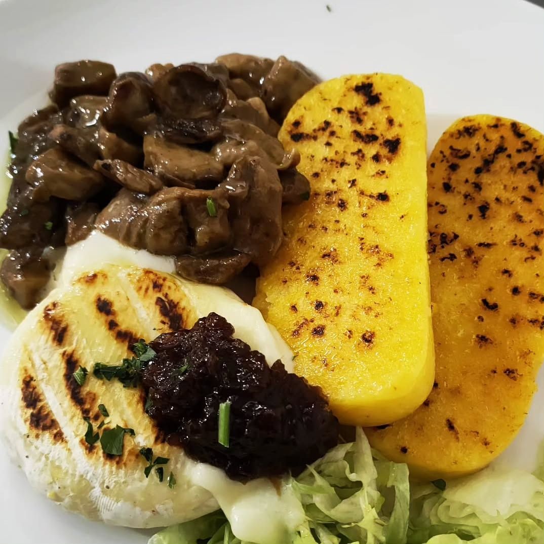 Piatto di cibo con funghi saltati, polenta grigliata, formaggio cremoso e una crema spalmabile scura.