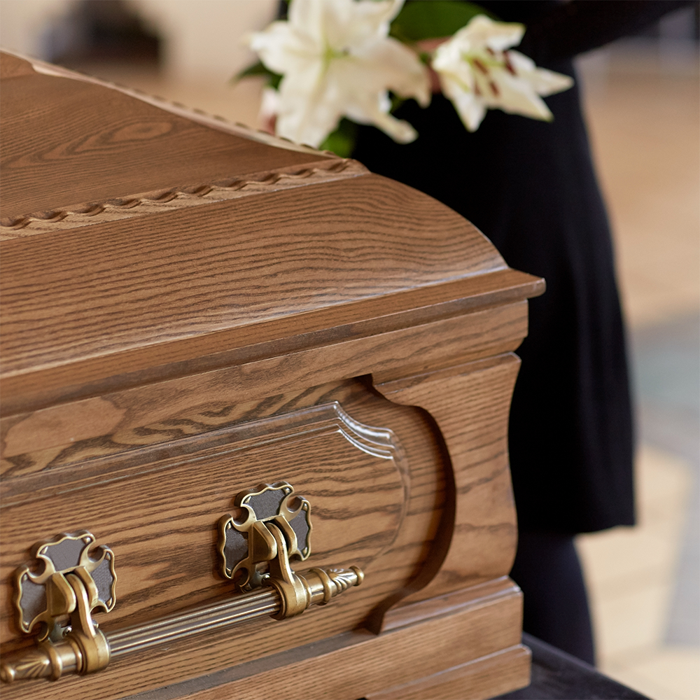 A close up of a wooden coffin with flowers in the background
