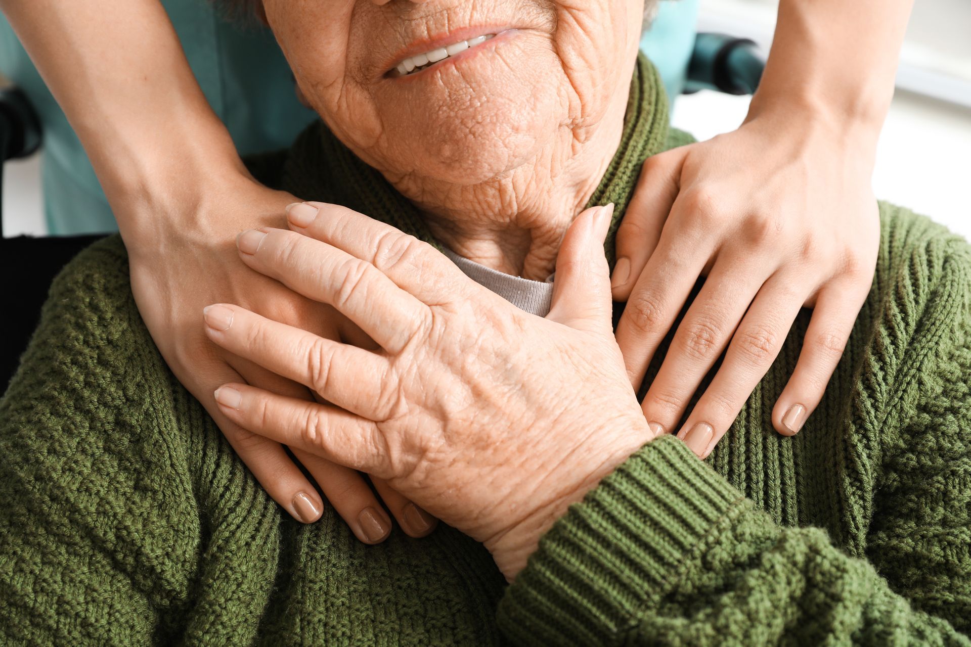 An elderly woman in a green sweater is being comforted by a nurse.