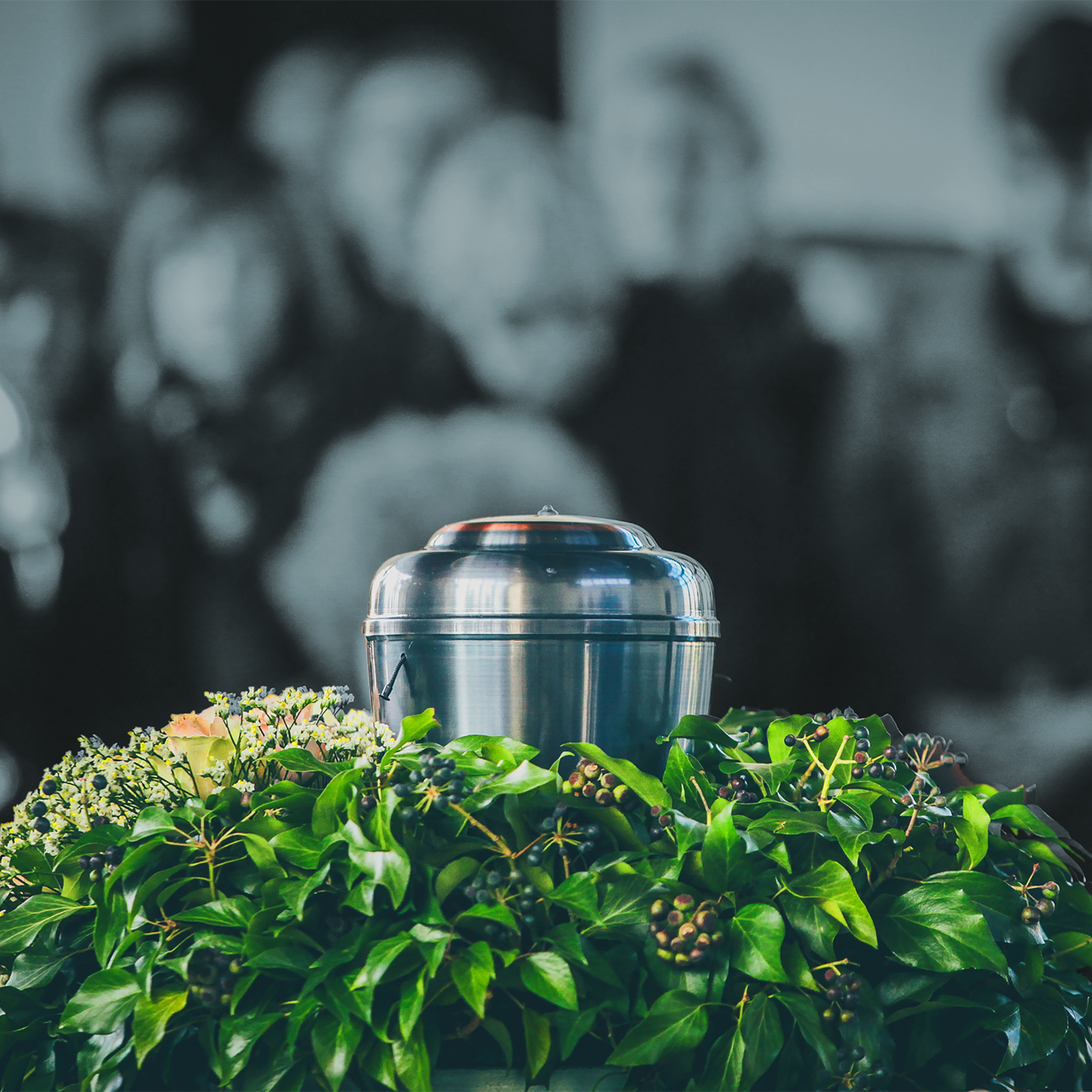 A metal urn is surrounded by green leaves and flowers.