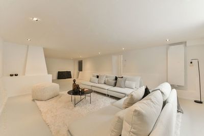 Lichte, minimalistische woonkamer met witte hoekbanken, open haard en grote ramen.