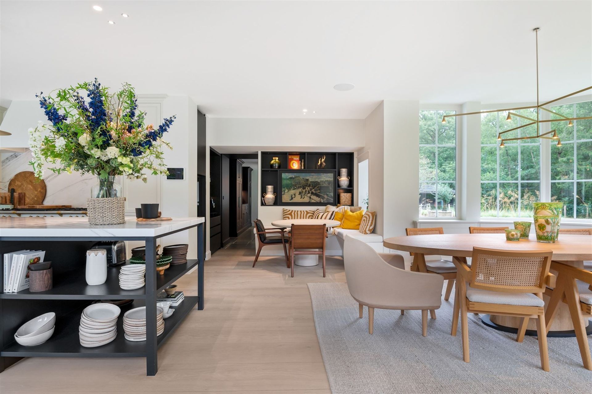 Een lichte, open eet- en keukenruimte met een groot kookeiland, een houten tafel en ingebouwde zitbanken.