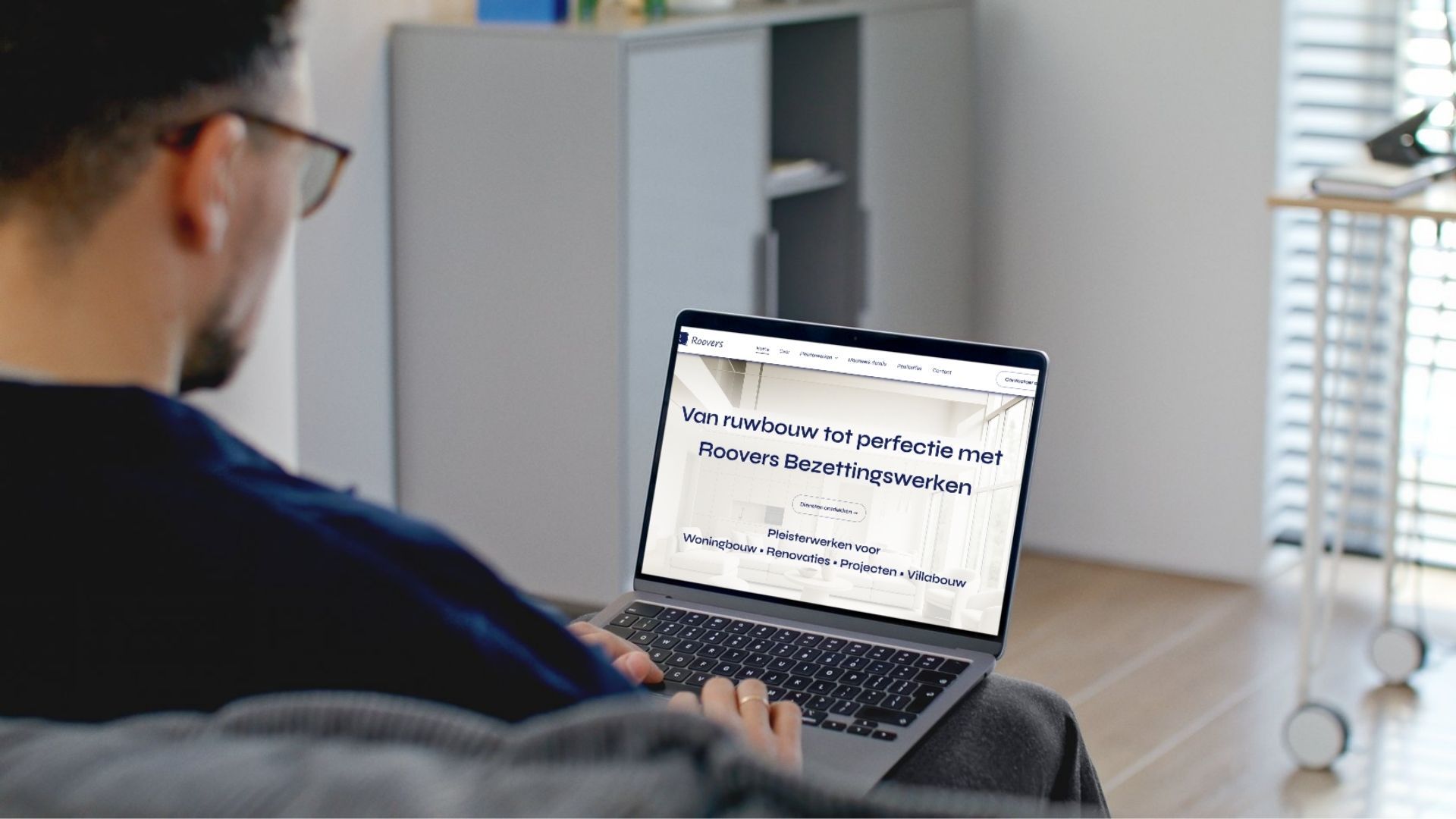 Een persoon die op een bank zit, kijkt naar een laptop waarop een website met tekst wordt weergegeven.