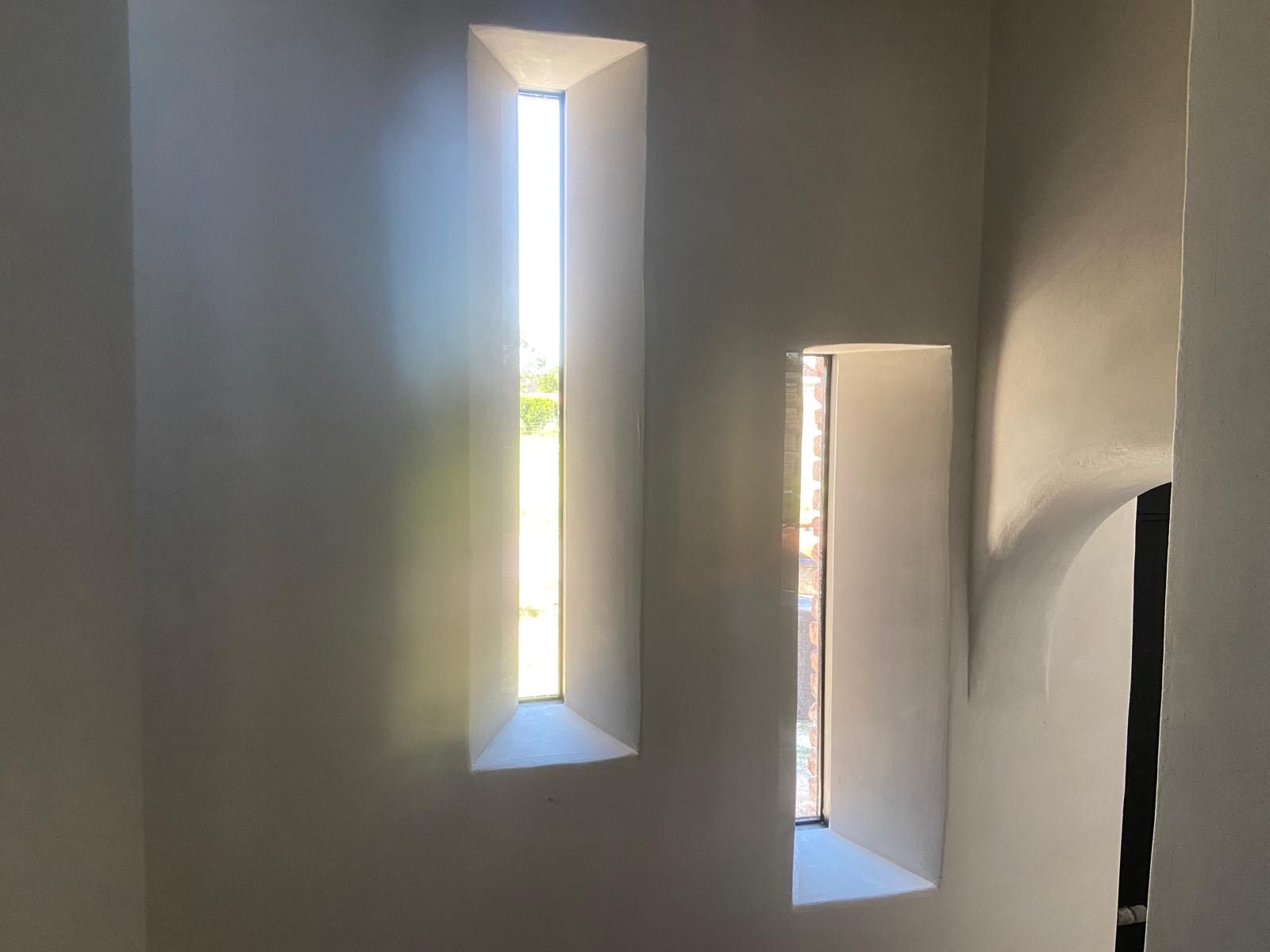 Twee smalle, rechthoekige ramen in dikke, gladde, witte binnenmuren laten natuurlijk licht binnen.