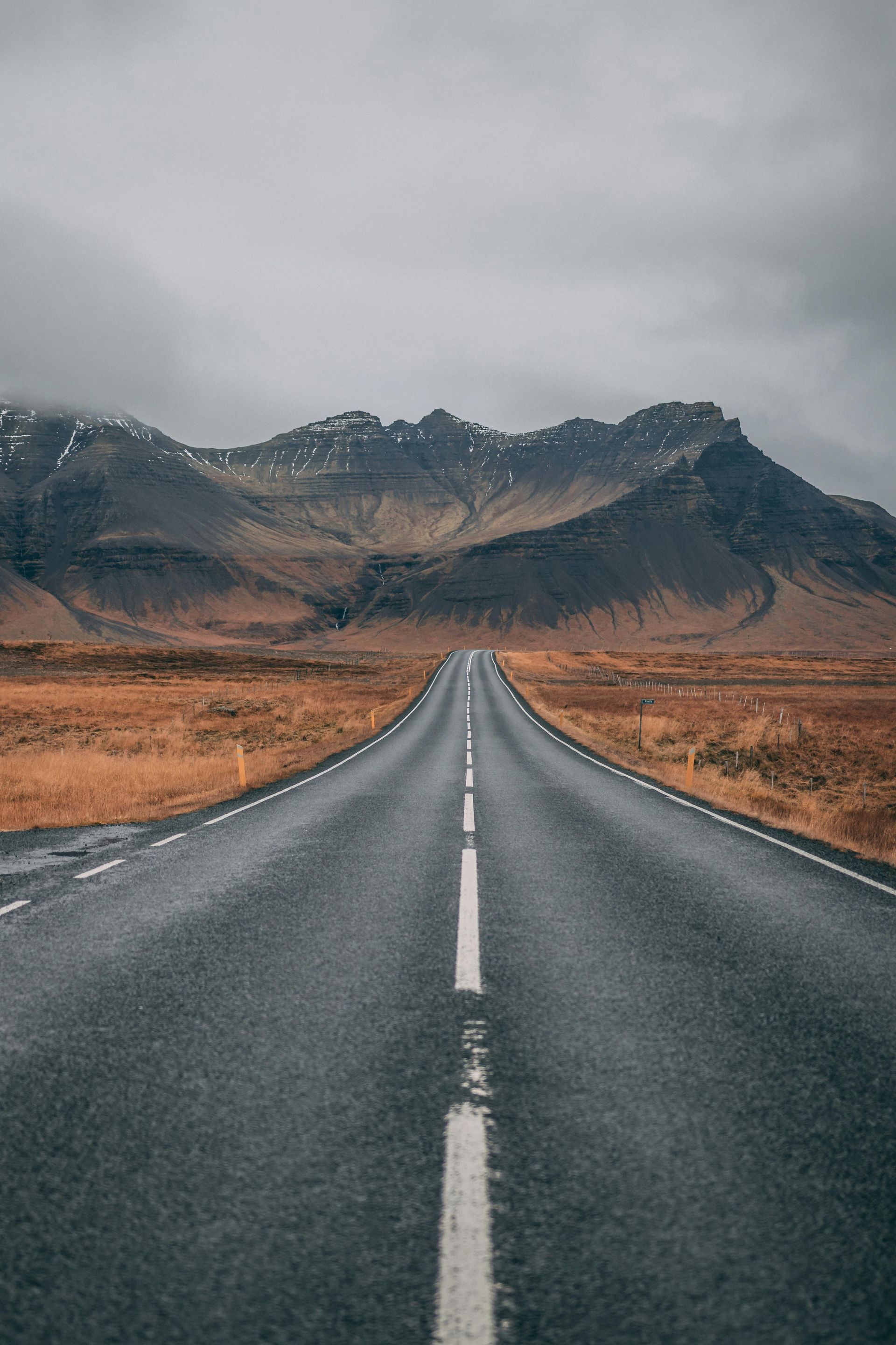 Road stretching towards mountain range under cloudy sky.