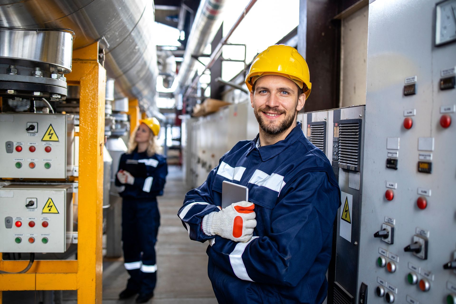A man in a hard hat is holding a tablet in a factory.