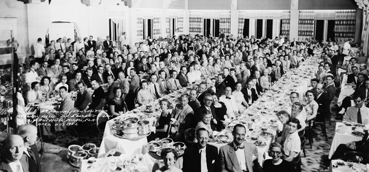 A large group of people are sitting at long tables in a room.