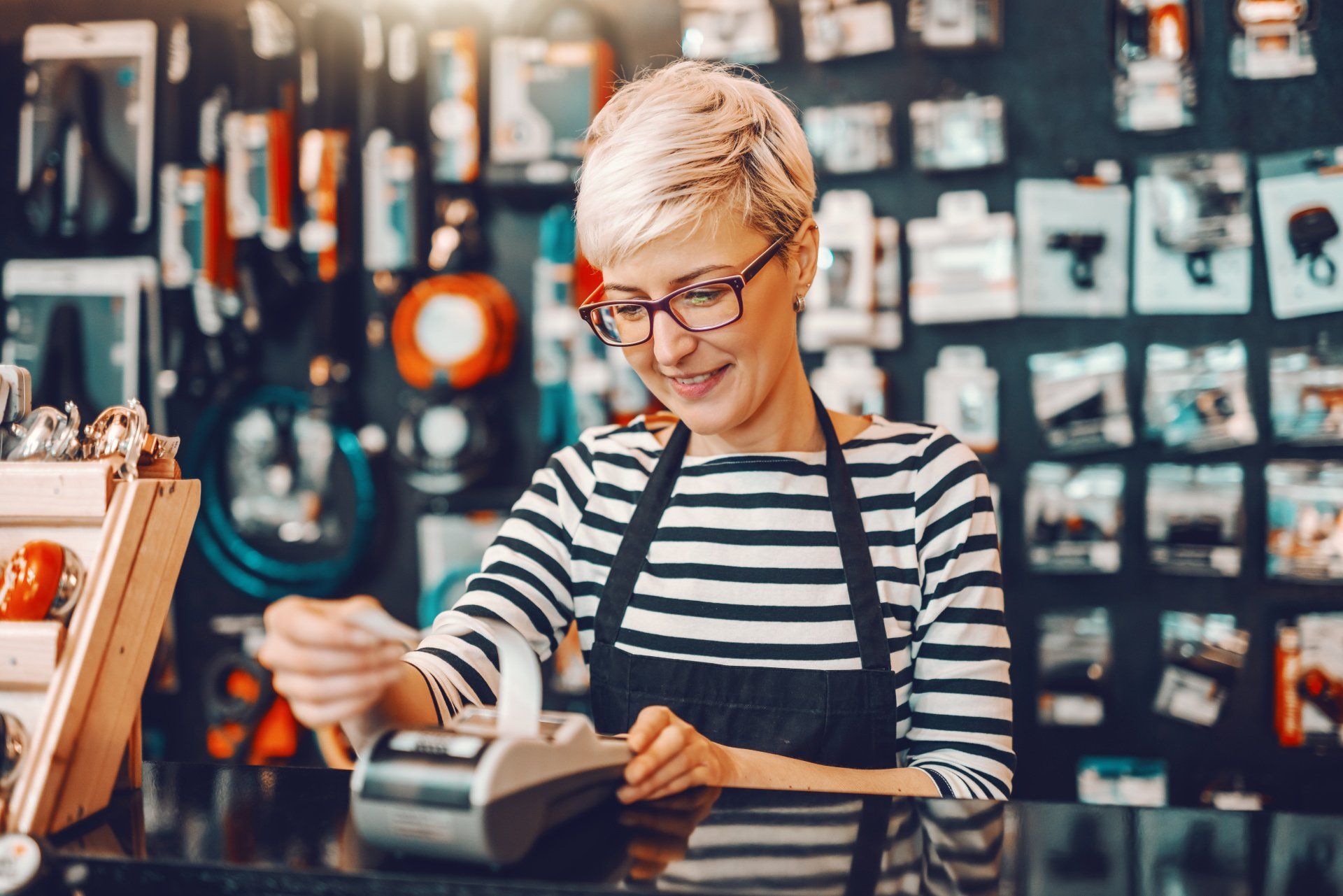 A woman is sitting at a counter in a store using a credit card.