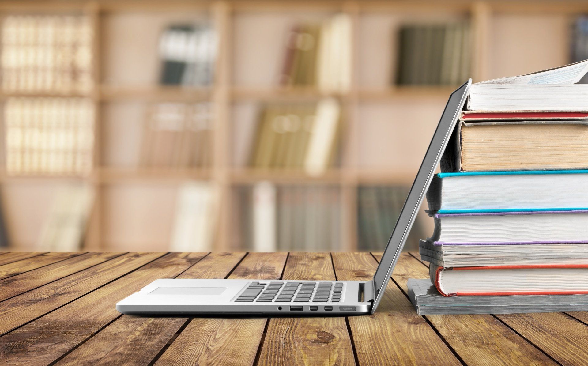 A laptop computer is sitting on a wooden table next to a stack of books.