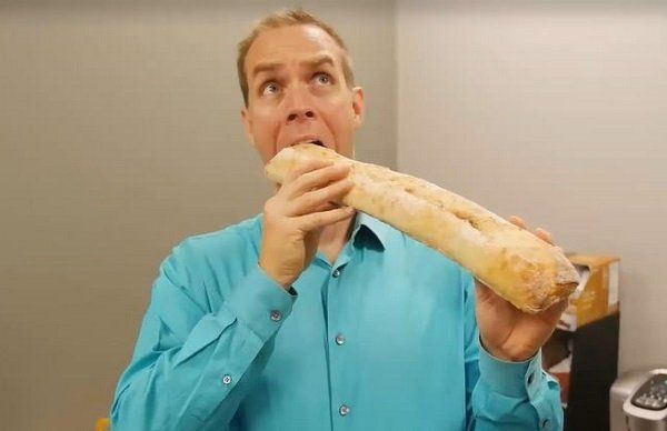 A man in a blue shirt is eating a long loaf of bread.