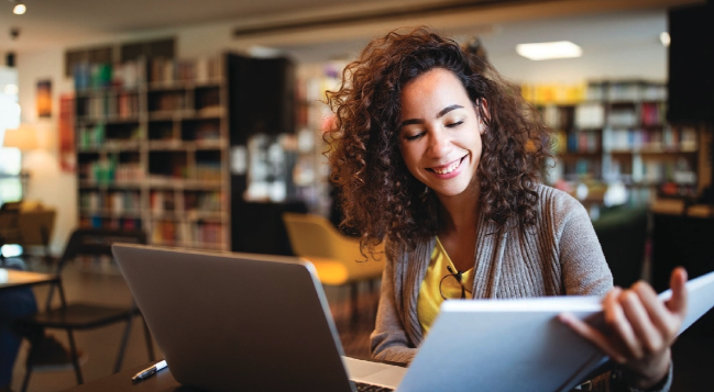 A woman is sitting at a table with a laptop and a book.