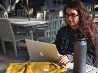 A woman is sitting at a table using an apple laptop