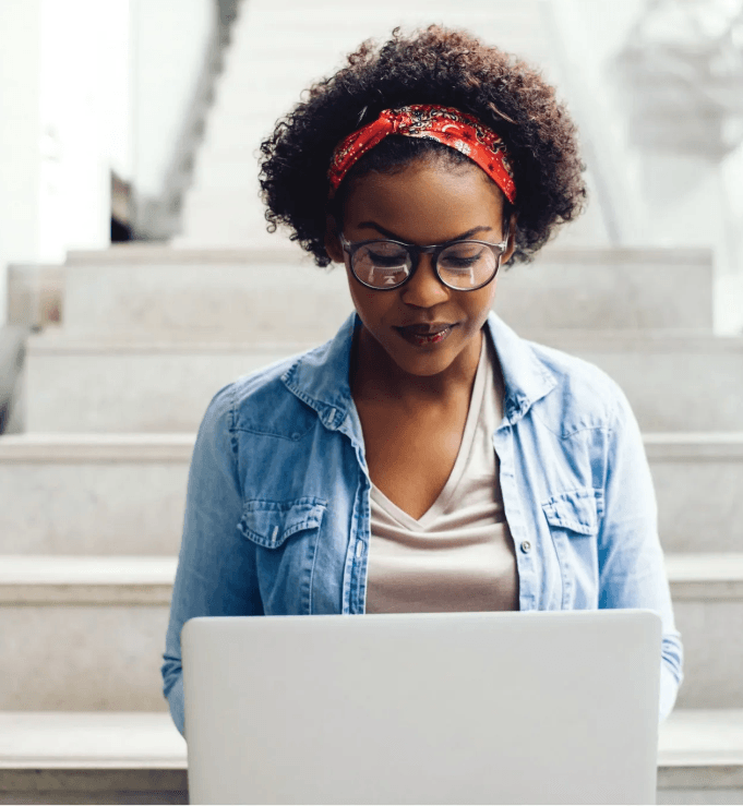 A woman wearing glasses is sitting on a set of stairs using a laptop computer.