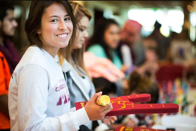 A woman in a white shirt is smiling while at a college game