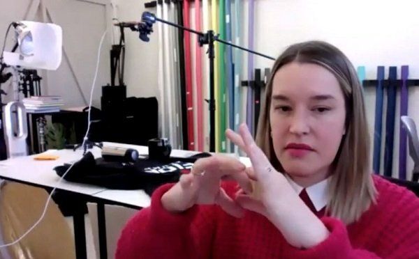 A woman in a red sweater is making a heart shape with her hands