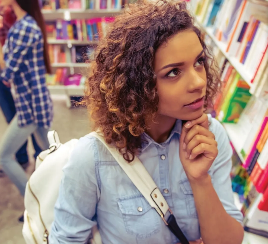 A woman with curly hair is sitting in a bookstore with a backpack.