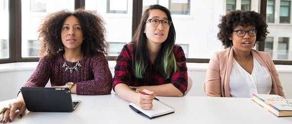 Three women are sitting at a table in front of a window.