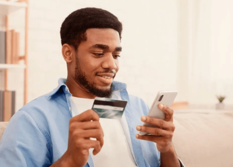 A man is holding a credit card and using a cell phone.