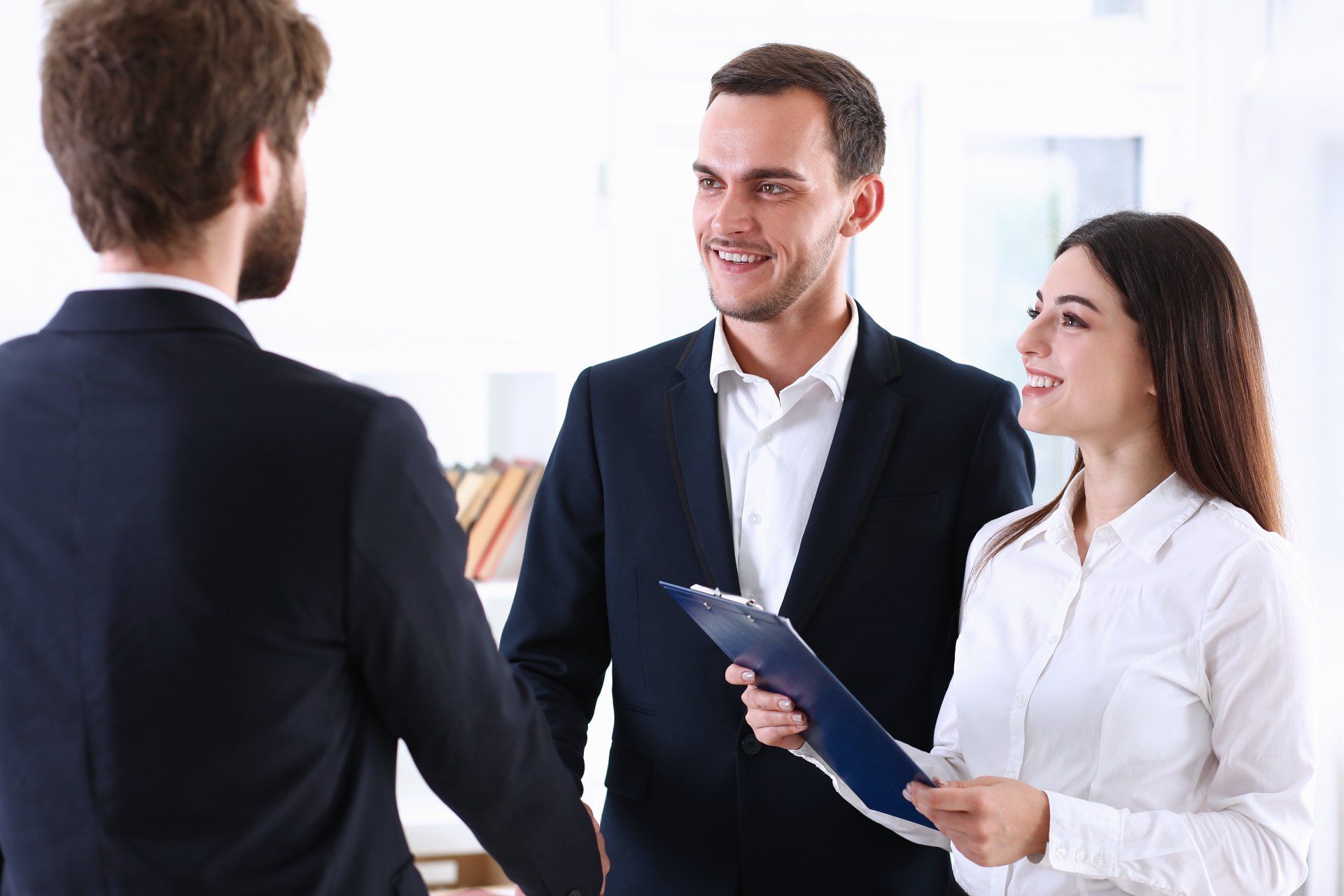 A man and a woman are shaking hands with a man in a suit.