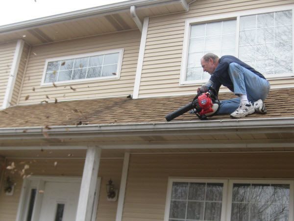 Man using leaf blower to clean house roof