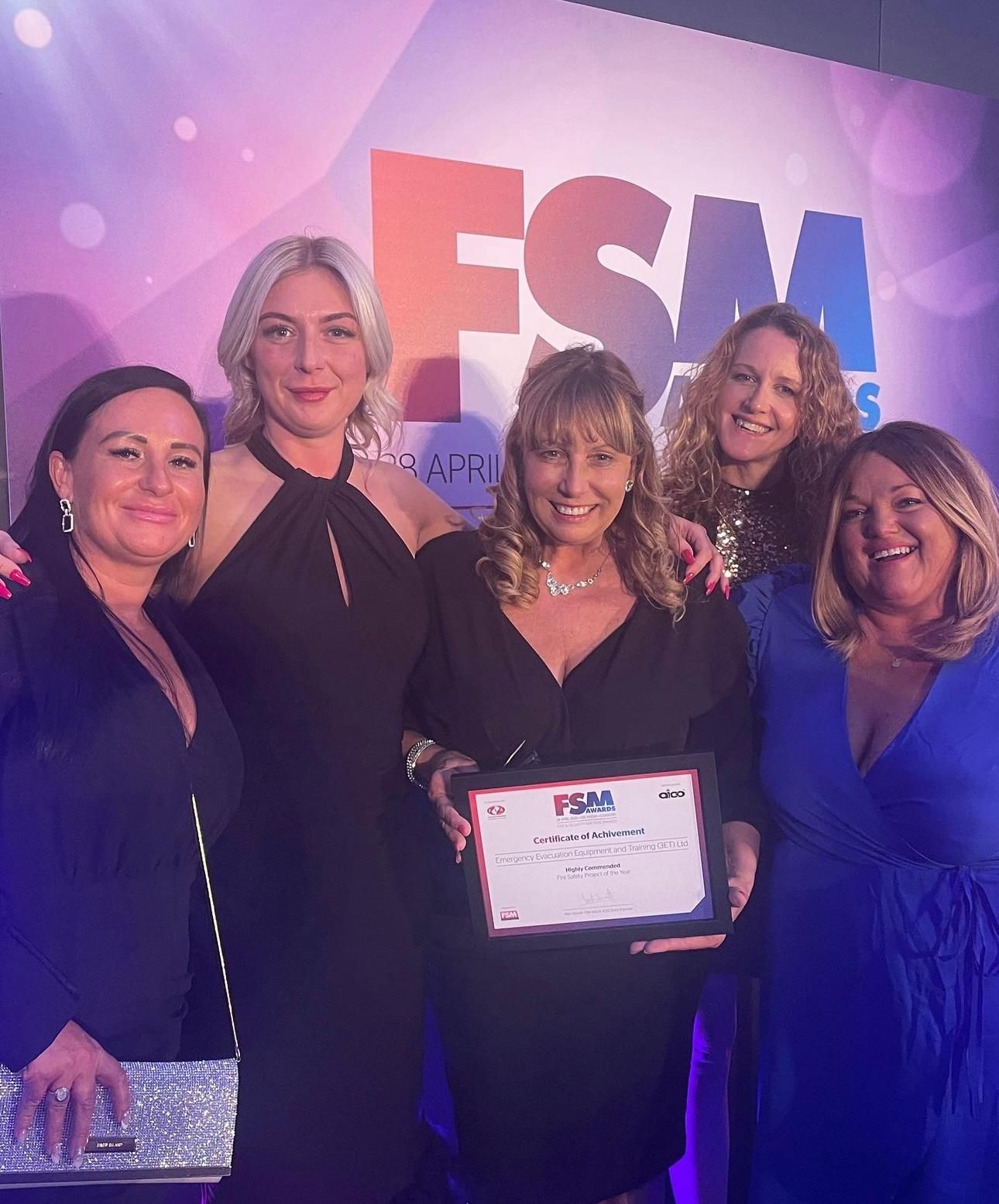 Five women in formal attire holding an award at an event with a