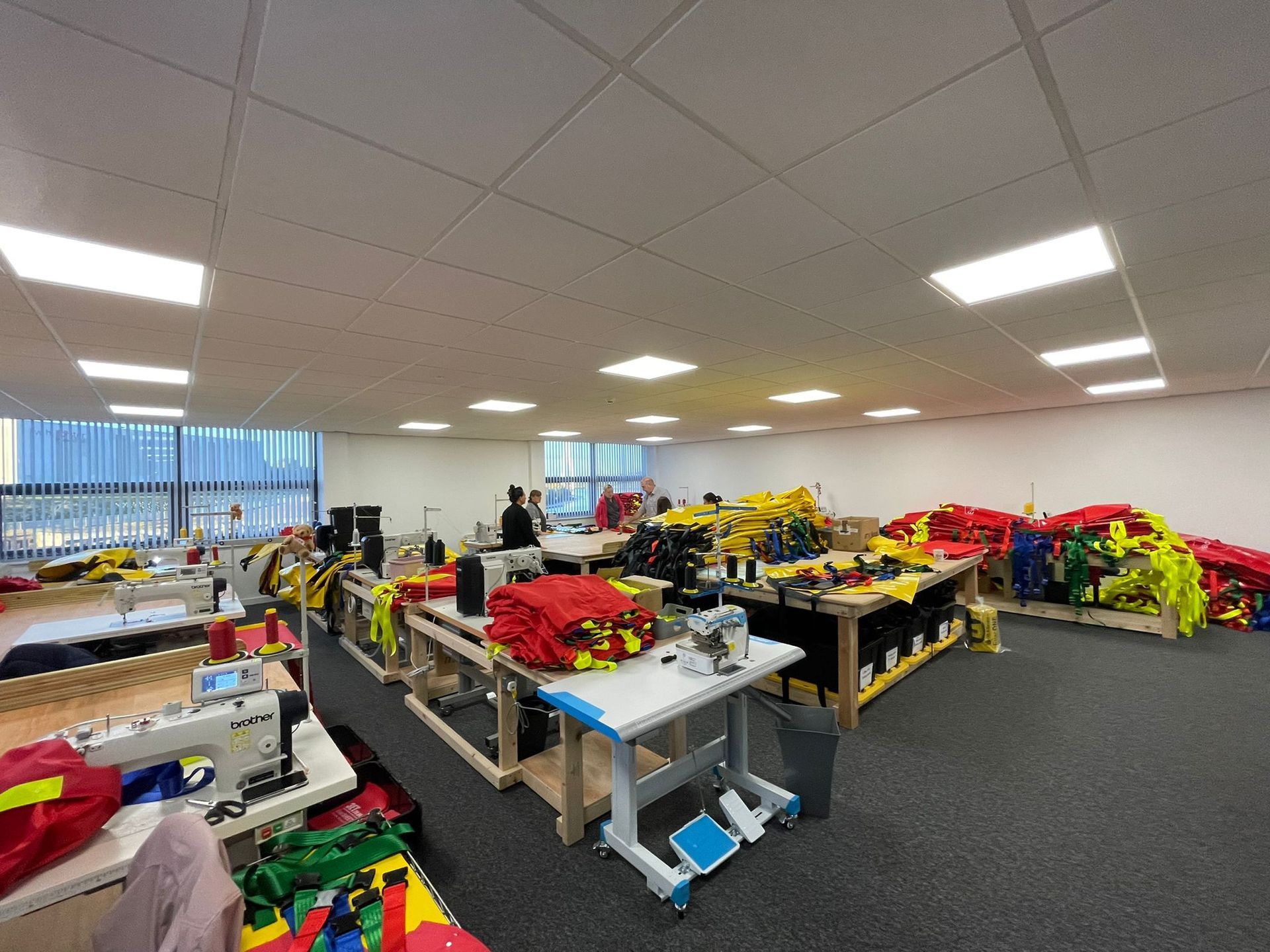 A brightly lit sewing room with sewing machines, work tables, and colorful fabric bundles.