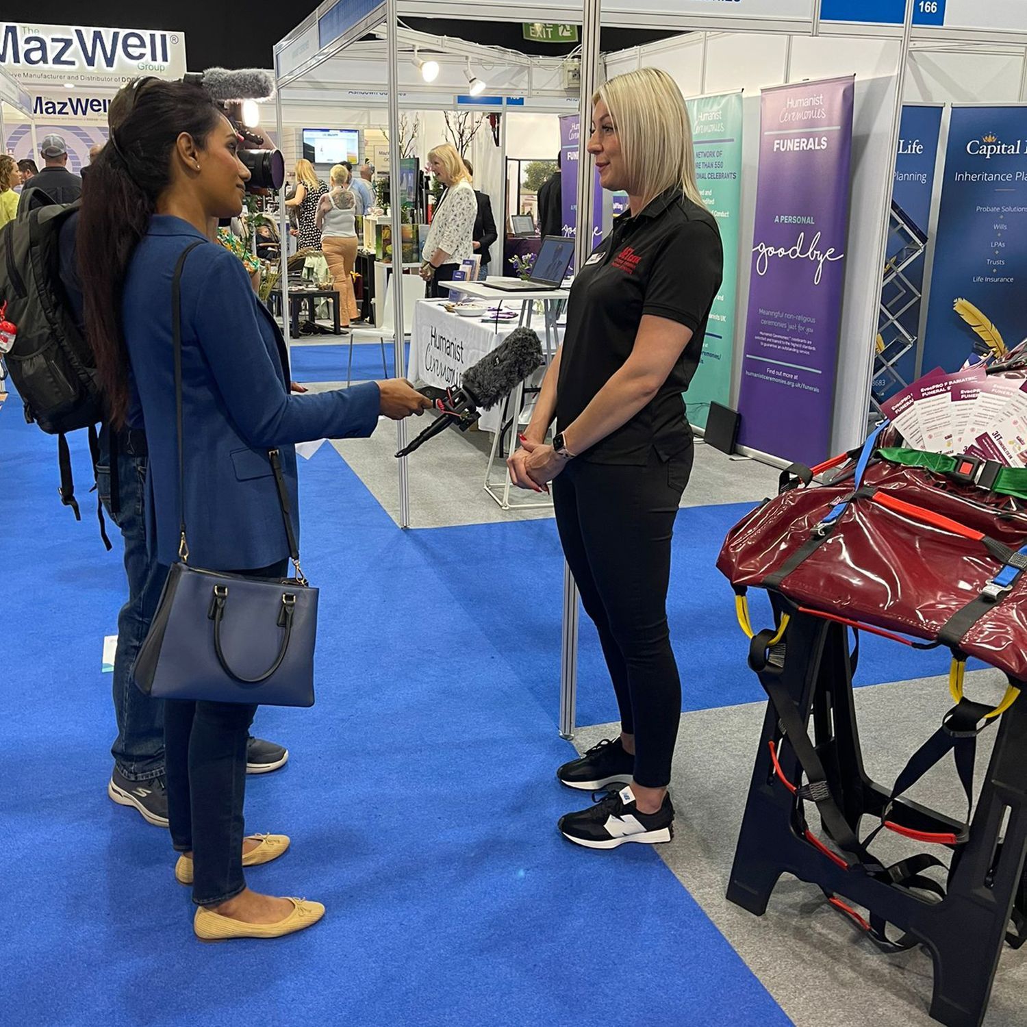 Woman interviewing another woman at a trade show. A saddle and equipment are visible.