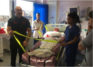 Medical staff practicing patient handling with yellow straps on a hospital bed.