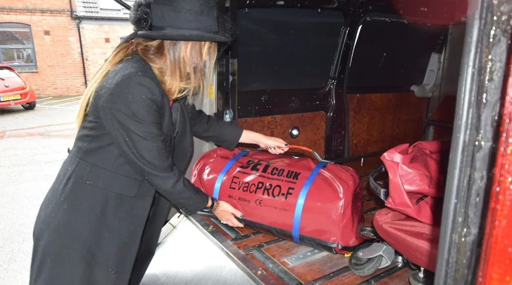 Woman in black coat and hat loading a red bag into a van.