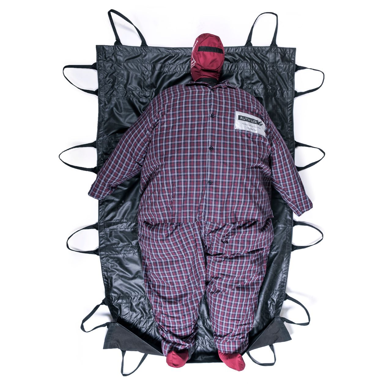A person in a checkered jumpsuit lies on a black stretcher with handles.