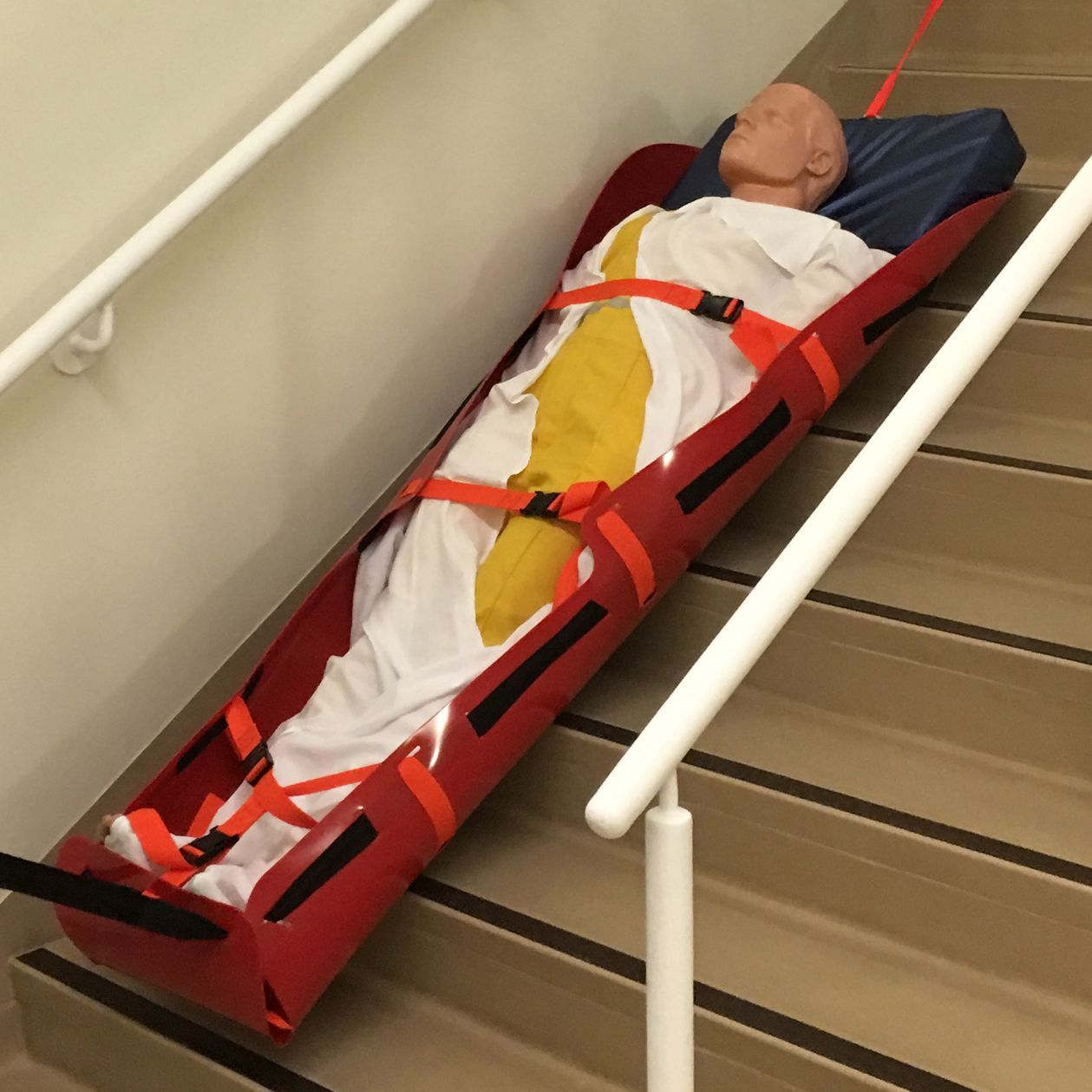 Mannequin in a red stair chair on stairs, secured with straps and ropes for transport.