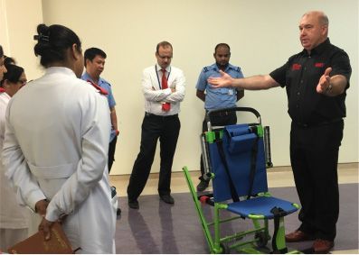 Man demonstrating use of a stair chair to a group of people indoors; medical training.